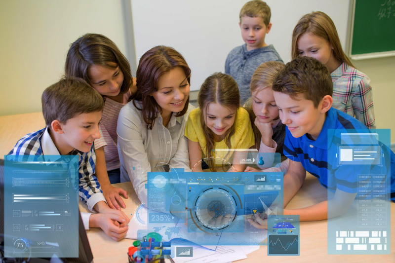 A smiling female teacher and a group of curious elementary students gathered around a table, interacting with a futuristic digital blue holographic interface.